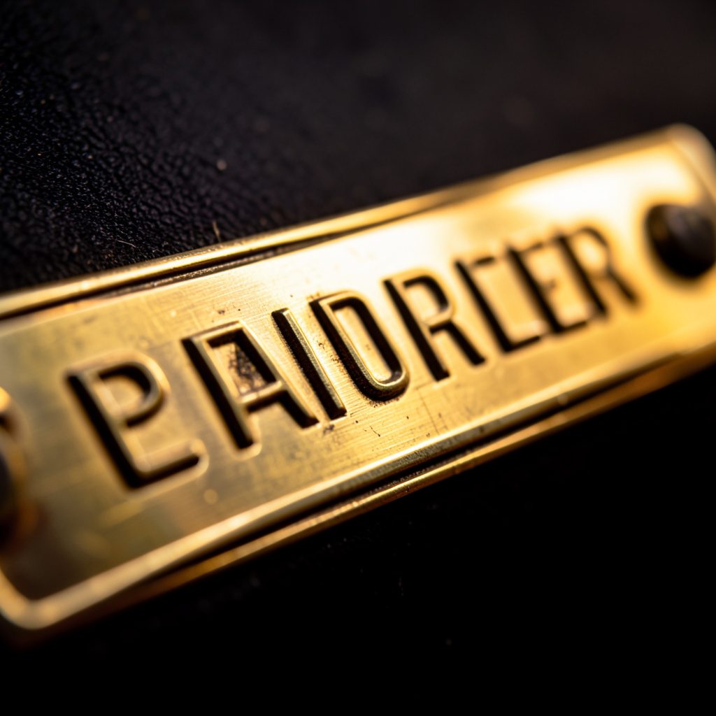 Extreme close-up of polished brass engine nameplate with engraved lettering, warm golden tones against dark background